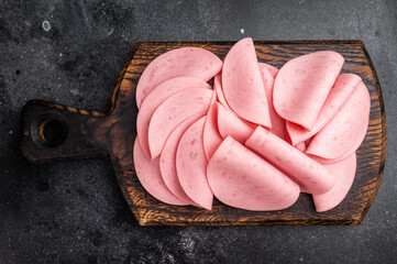Overhead view of cold cuts (mortadella) on a small wooden board. Gourmet deli concept on a dramatic, black texture background. © Mironov