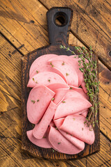 Slices of pink bologna lunch meat served on a rustic dark wooden cutting board. Dark, moody background with copy space. © Mironov