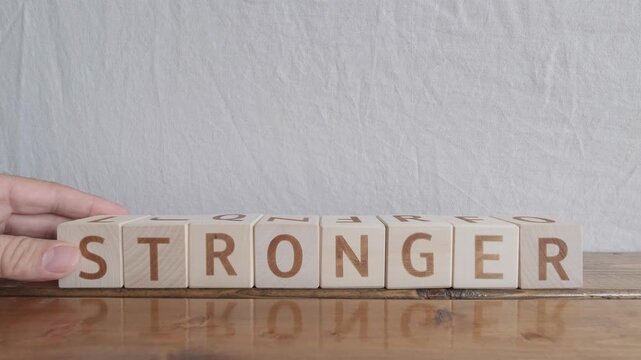 motivational word Stronger, laying out by hand from letters on wooden cubes, slow motion
