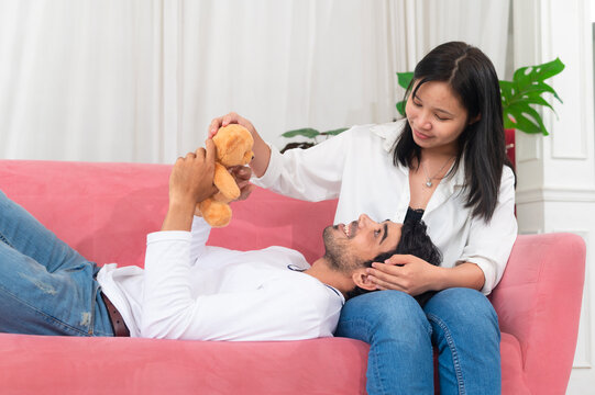 A couple enjoys a playful moment on a couch, sharing laughter and affection with a teddy bear, showcasing love and connection in a cozy setting.