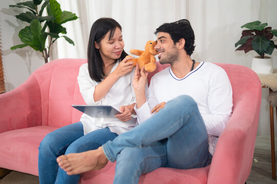 A joyful couple enjoys their time together on a cozy couch, playfully interacting with a plush toy, showcasing love and togetherness.