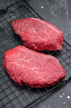 Raw Wagyu top blade steaks with rich marbling on metal grate next to red pepper and vintage fork over dark stone surface perfect for gourmet stock images.