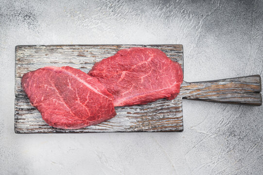 Fresh raw Wagyu chuck steak resembling zabuton or Denver cut arranged with herbs on weathered wood against bright gray backdrop ideal for premium food photography.