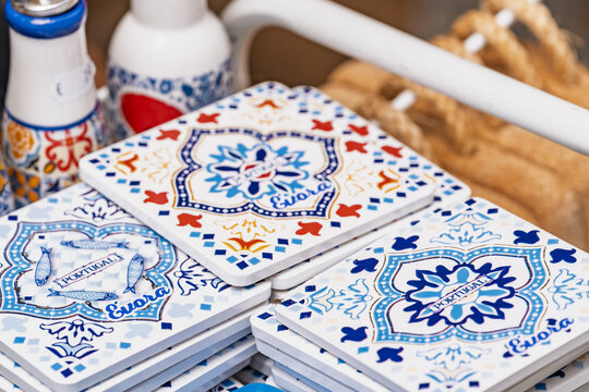 View of decorative ceramic tiles featuring traditional blue and white patterns, fish motifs, and the names Evora and Portugal, stacked on a display rack in Evora, Evora District, Portugal.