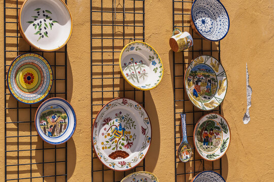 View of decorative hand-painted ceramic plates and pottery displayed on a metal grid against a warm yellow wall in Evora, Evora District, Portugal.