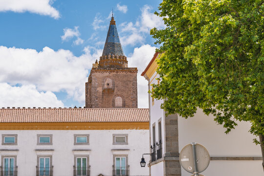 View of the historic Cathedral of Evora with its iconic blue tiled spire rising above traditional white buildings and lush greenery in Evora, Evora District, Portugal.