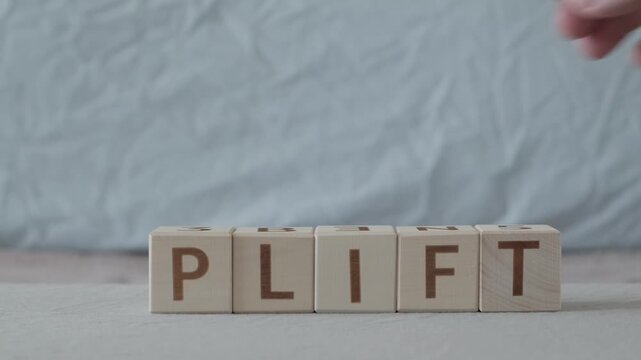 motivational word Uplift, laying out  by hand from letters on wooden cubes, slow motion