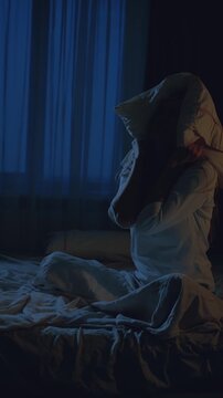 Sad woman unable sleep suffering from headache, covers head with pillow falls asleep on bed, dark room night light. Pain migraine. girl chronic tiredness feels bad, noisy neighbors vertical video crop