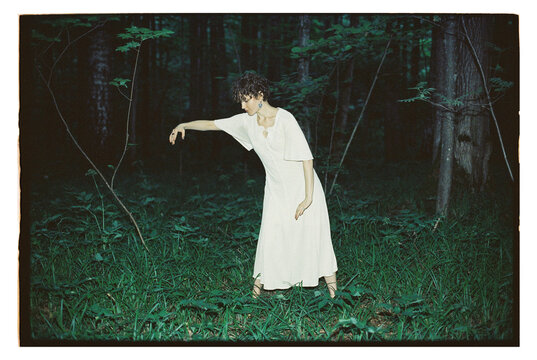 Girl in a forest reaching out in a dress at dusk