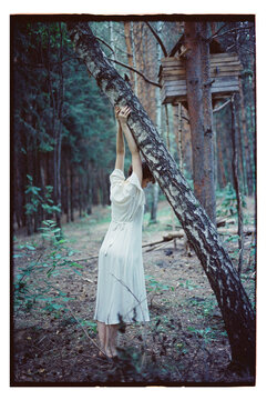 Girl in a forest hanging from a tree with a small house above
