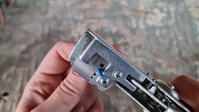 The process of stripping insulation from a blue wire using an automatic stripper. Hands of a craftsman using a professional pliers tool to remove the insulation from a copper electrical cable