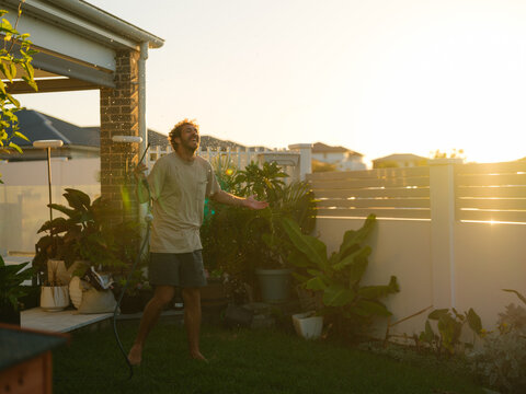 Man laughs with open arms spraying the yard at sunset