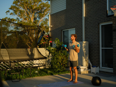 A man doing dumbbells curls on a backyard patio