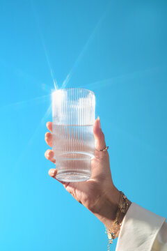 Hand holding a glass of water against a clear blue sky