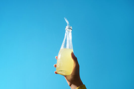 A refreshing glass bottle of lemonade is held up against a bright sky