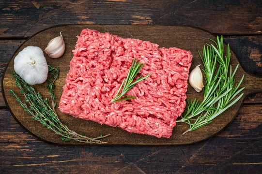Raw lamb and beef forcemeat with rosemary and garlic on dark wood surface ideal for culinary, kitchen and ingredient stock photography.