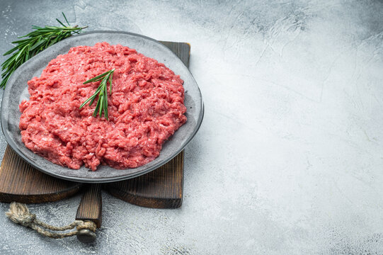 Ground lamb and beef raw meat on gray dish with rosemary against textured concrete backdrop offering detailed texture perfect for grocery and cooking imagery.