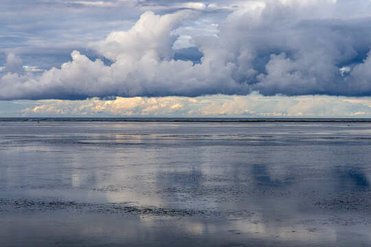 View of the calm, reflective surface of a shallow bay under a dramatic, cloud-filled sky in Allingabro, Jutland, Denmark.