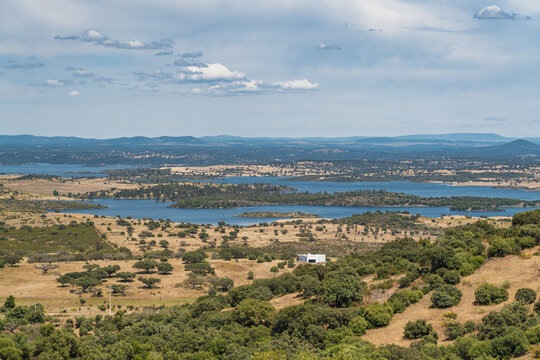 View of the Alqueva reservoir surrounded by rolling hills, cork oak trees, and dry landscape under a blue sky in Monsaraz, Evora District, Portugal.