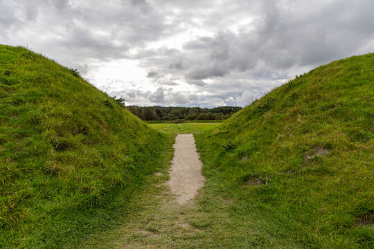 View of the grassy earthen ramparts and central path at The Viking Museum Fyrkat, a historic Viking ring fortress site under a cloudy sky in Hobro, Jutland, Denmark.