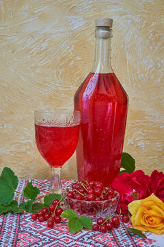 Homemade redcurrant wine in a glass bottle and a glass. Redcurrant liqueur on an embroidered tablecloth