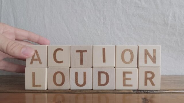 motivational word Action louder, laying out by hand from letters on wooden cubes, slow motion
