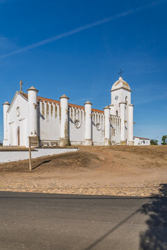 View of the historic Church of Minas de Sao Domingos with its distinctive white walls and cylindrical buttresses under a clear blue sky in Corte do Pinto, Beja District, Portugal.
