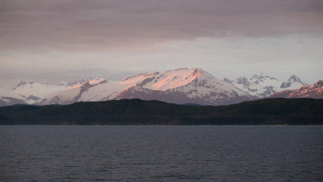 Breathtaking Alaska mountain glacier range view seen from outdoor deck of cruise ship liner sailing the Inside Passage transit with spectacular landscape scenery during sunset