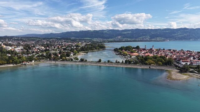 Aerial panoramic view of Lindau Island on Lake Constance in Bavaria, Germany, with the historic old town, marina, waterfront and green Alpine foothills under a dramatic summer sky.