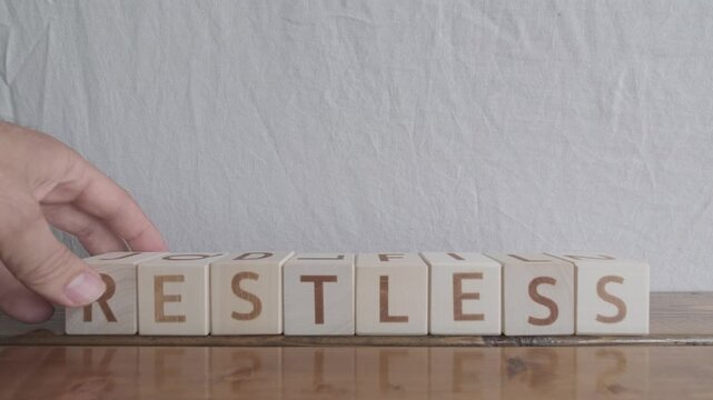 motivational word Restless, laying out by hand from letters on wooden cubes, slow motion
