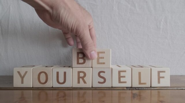 motivational word Be yourself, laying out by hand from letters on wooden cubes, slow motion
