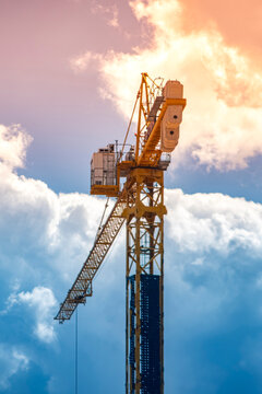 Yellow tower crane top against dramatic blue and orange sunset sky. Use for construction industry, infrastructure development, real estate, and engineering project content.