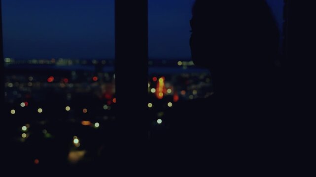 black silhouette face of mystery woman standing looking at window night city light bokeh blue sky, mood depression sadness loneliness emotion. Adult sad girl back rear view enjoy view. dark home room.