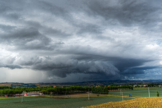 View of a dramatic shelf cloud looming over the rural landscape with agricultural fields and trees in Corridonia, Marche, Italy.