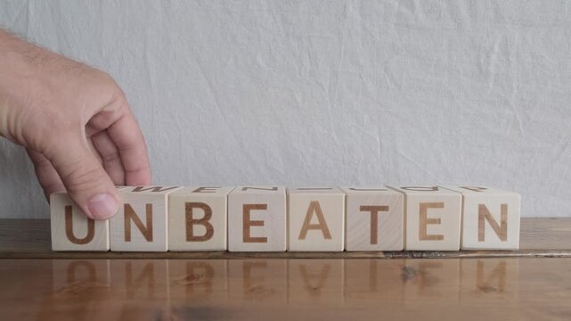 motivational word Unbeaten, laying out by hand from letters on wooden cubes, slow motion

