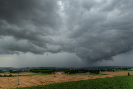 View of dark storm clouds gathering over the rural agricultural fields and rolling hills of Corridonia, Marche, Italy.