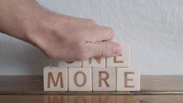 motivational word One more, laying out by hand from letters on wooden cubes, slow motion
