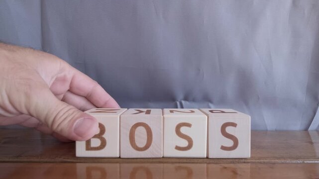 motivational word Boss, laying out by hand from letters on wooden cubes, slow motion
