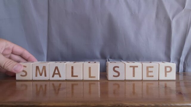 motivational word Small step, laying out by hand from letters on wooden cubes, slow motion
