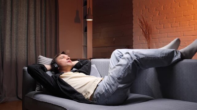 Young man in headphones relaxing on a cozy sofa in his living room, enjoying music and quiet downtime, unwinding and soaking in a peaceful, comfortable moment at home