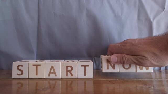 motivational word Start now, laying out by hand from letters on wooden cubes, slow motion
