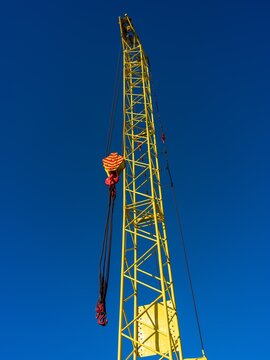 View of a tall yellow construction crane with a hook and cables set against a clear blue sky in Klaipeda, Klaipeda County, Lithuania.