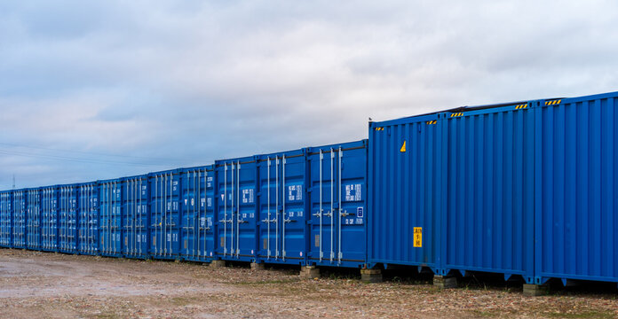 View of a long row of blue shipping containers stored in the port area under a cloudy sky in Klaipeda, Klaipeda County, Lithuania.