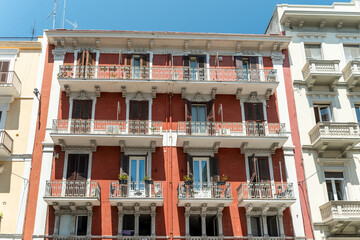 Elegant red and cream apartment building with ornate balconies, wrought iron railings and potted plants on every floor under a clear blue sky, concept of mediterranean architecture, city living and h © daily_creativity