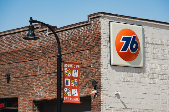 Downtown Eau Claire, WI - Sep 3, 2026: A vintage 76 gas station sign on a brick commercial building in downtown and a decorative lamppost banner.