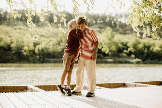 Joyful siblings sharing a warm moment near a tranquil lakeside setting