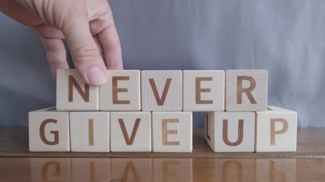 motivational word Never give up, laying out by hand from letters on wooden cubes, slow motion
