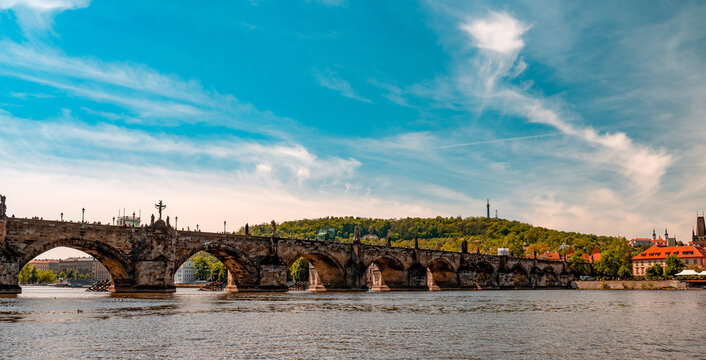 View of the historic Charles Bridge spanning the Vltava River with the city skyline in the background under a bright blue sky in Prague, Prague, Czechia.