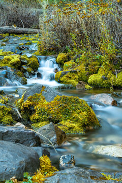 View of a long exposure of a creek flowing over moss-covered rocks through the Uinta Mountains during autumn in American Fork, Utah, United States.