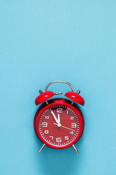 Vertical New Year countdown background with red vintage alarm clock showing five minutes to midnight on light blue backdrop. Minimalist festive winter holiday flat lay with large copy space.